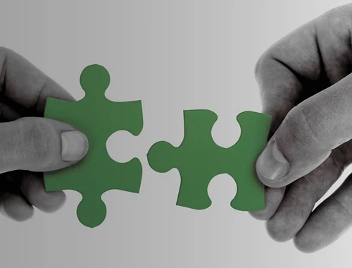 Two hands fitting green puzzle pieces together